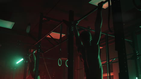 adult-athletes-are-training-in-gym-in-darkness-man-and-woman-are-jumping-and-doing-pull-ups